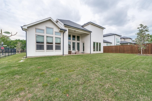 back of house featuring fence, a yard, and stucco siding