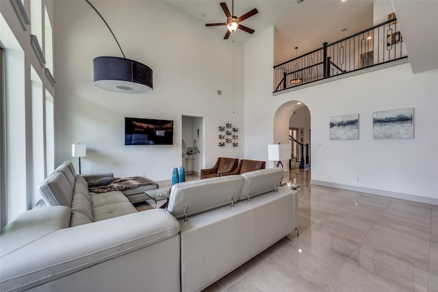 living room with ceiling fan, a high ceiling, baseboards, and arched walkways