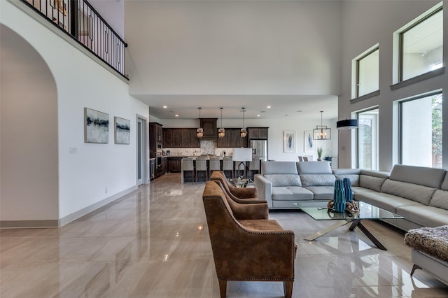 living room with a high ceiling, arched walkways, marble finish floor, and baseboards