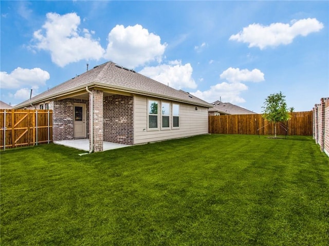 rear view of property with a fenced backyard, brick siding, roof with shingles, a patio area, and a lawn