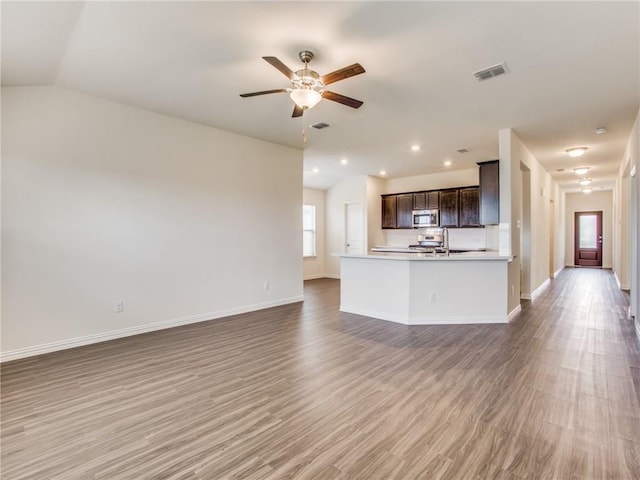 unfurnished living room with a ceiling fan, visible vents, wood finished floors, and baseboards