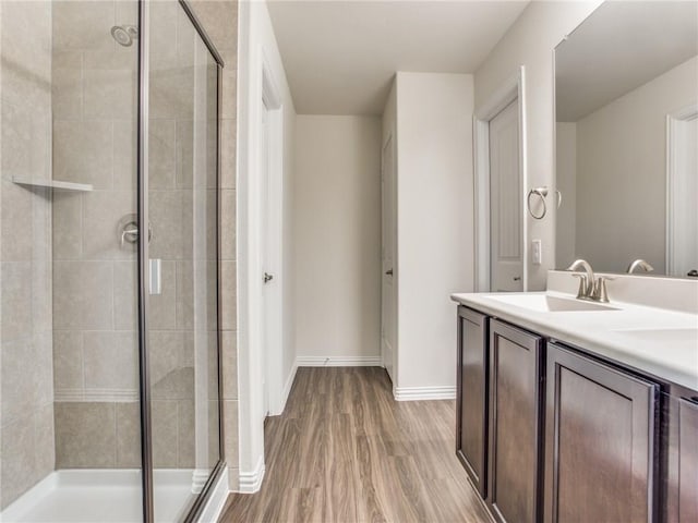 bathroom with wood finished floors, baseboards, a stall shower, and a sink