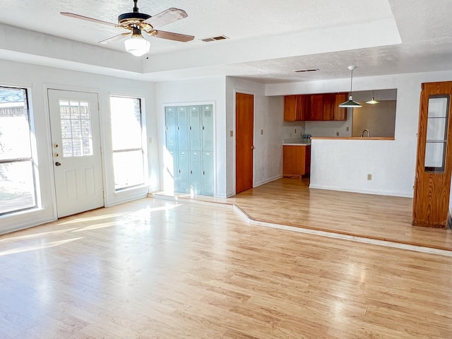 505 N Yosemite, Iowa Park, TX 76367 - unfurnished living room featuring light wood-style floors, ceiling fan, baseboards, visible vents, and a raised ceiling