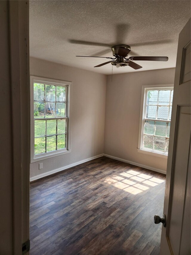 empty room with a textured ceiling, dark wood-style flooring, ceiling fan, and baseboards