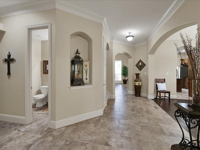 hallway featuring crown molding, stone finish flooring, arched walkways, and baseboards