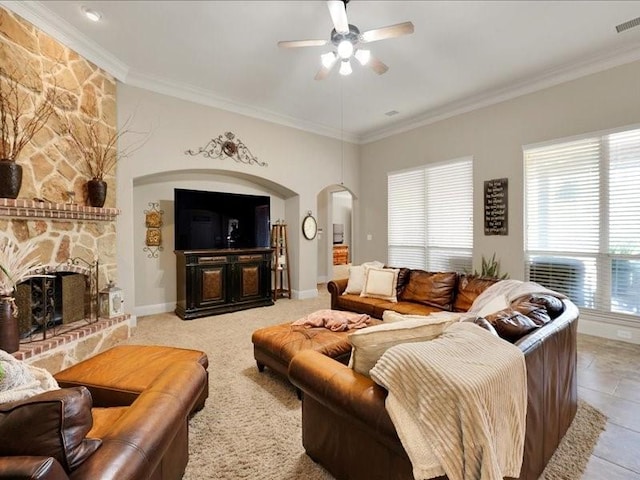 tiled living area featuring ceiling fan, a stone fireplace, baseboards, ornamental molding, and arched walkways