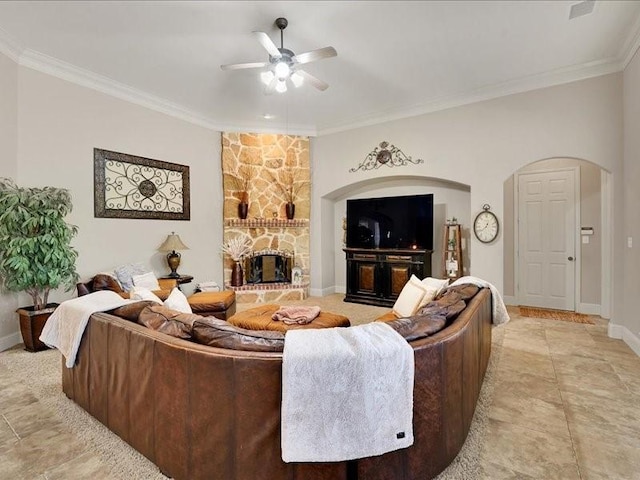 living room featuring crown molding, a ceiling fan, arched walkways, and a stone fireplace
