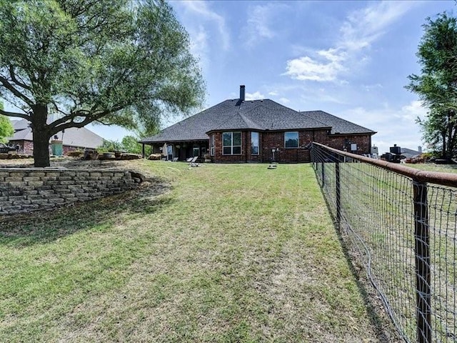 rear view of property featuring fence, a yard, and brick siding