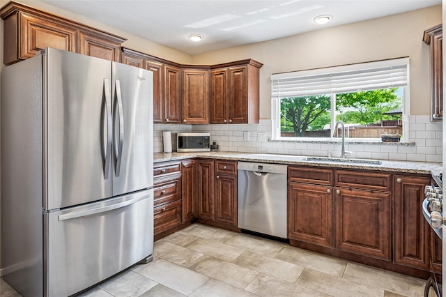 kitchen with appliances with stainless steel finishes, light stone counters, tasteful backsplash, and a sink