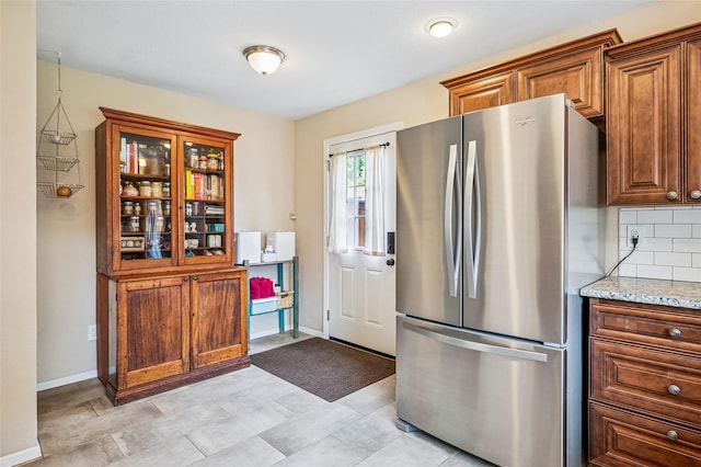 kitchen with light stone countertops, decorative backsplash, freestanding refrigerator, and baseboards