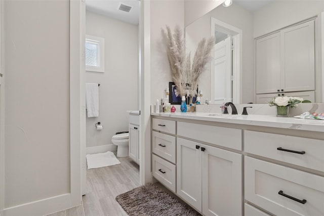 bathroom featuring vanity, toilet, visible vents, baseboards, and wood finished floors