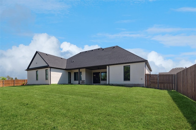 back of house featuring a lawn, stucco siding, a fenced backyard, and roof with shingles