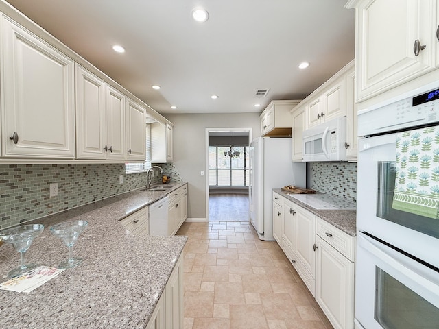 kitchen with a sink, stone tile floors, tasteful backsplash, visible vents, and white appliances