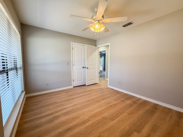 unfurnished bedroom featuring a ceiling fan, visible vents, light wood-style flooring, and baseboards