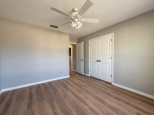 unfurnished bedroom with a closet, visible vents, wood finished floors, and baseboards