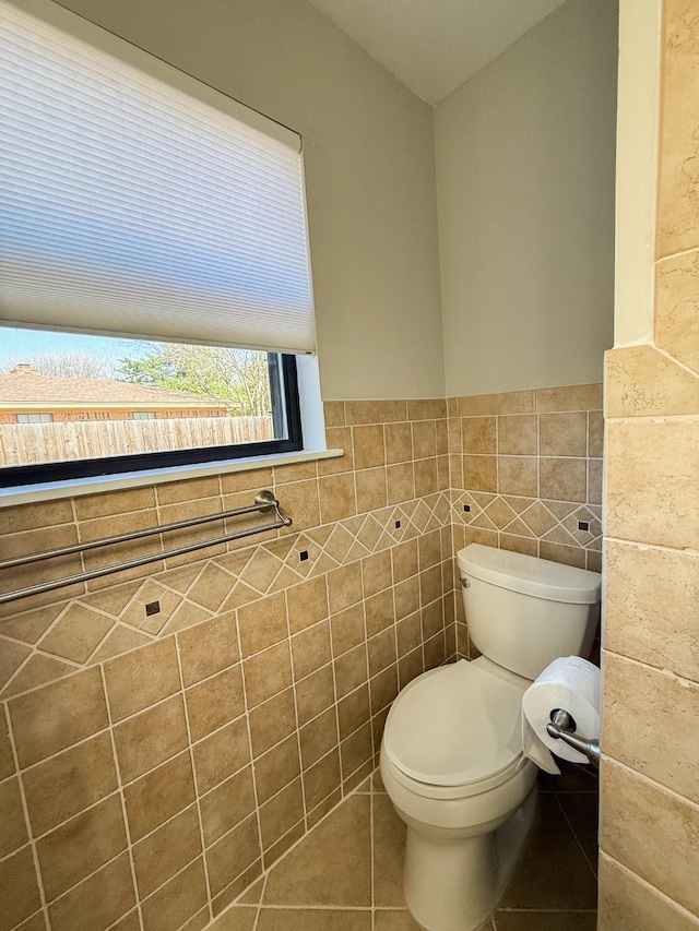 half bathroom with tile patterned floors, toilet, a wainscoted wall, and tile walls