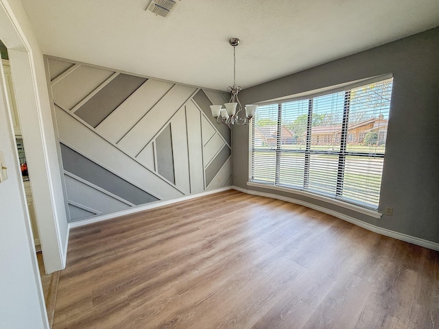 unfurnished dining area with visible vents, wood finished floors, a chandelier, and baseboards
