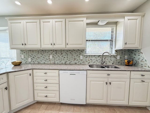 kitchen with tasteful backsplash, light stone countertops, white dishwasher, and a sink