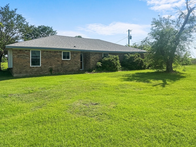 back of property with a yard, brick siding, and roof with shingles