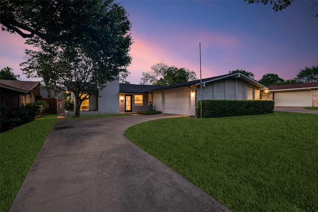 view of front of home featuring concrete driveway, a yard, a garage, and brick siding