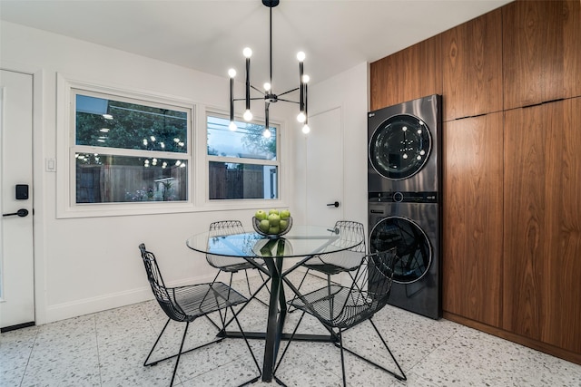 dining area featuring light floors, stacked washing maching and dryer, a chandelier, and baseboards