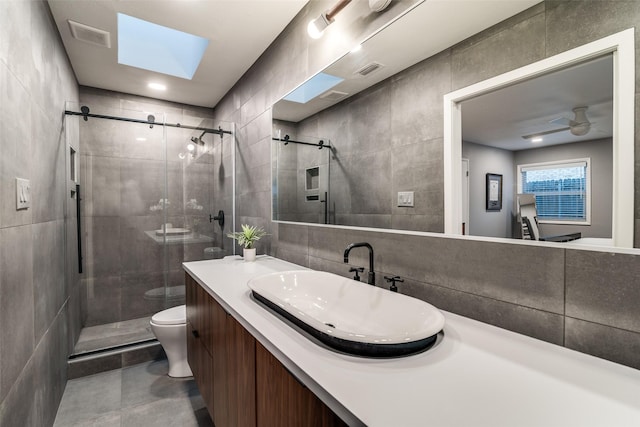 full bathroom featuring a shower stall, toilet, tile walls, vanity, and a skylight