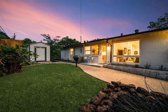 back of house at dusk with a patio area, an outbuilding, a yard, a storage unit, and fence