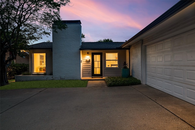 exterior space with driveway, a chimney, a shingled roof, brick siding, and a garage