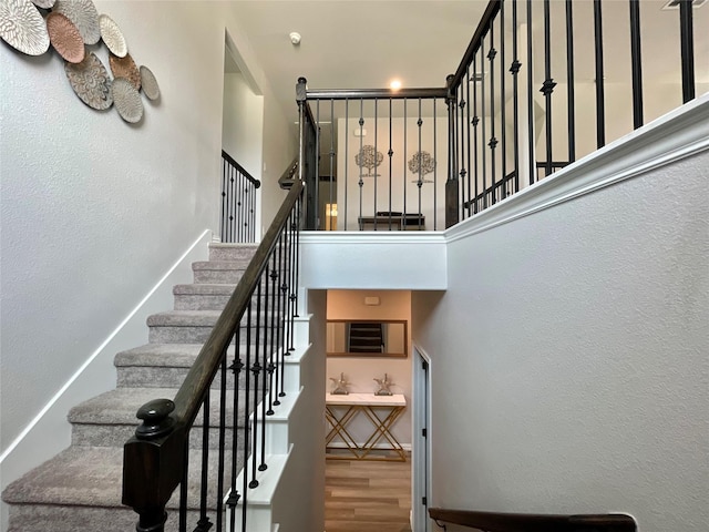 stairs with a high ceiling, a textured wall, and wood finished floors