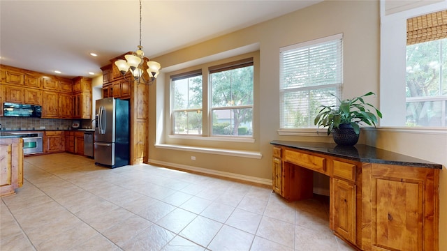 kitchen with brown cabinets, an inviting chandelier, decorative backsplash, light tile patterned floors, and appliances with stainless steel finishes