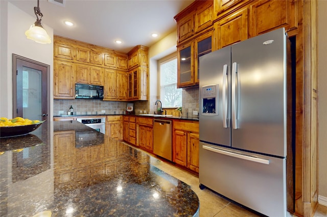kitchen featuring stainless steel appliances, tasteful backsplash, dark stone counters, decorative light fixtures, and glass insert cabinets