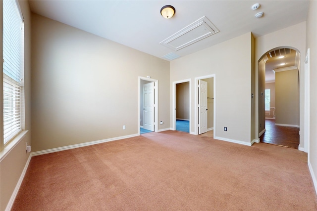 unfurnished bedroom with attic access, light carpet, a spacious closet, arched walkways, and baseboards
