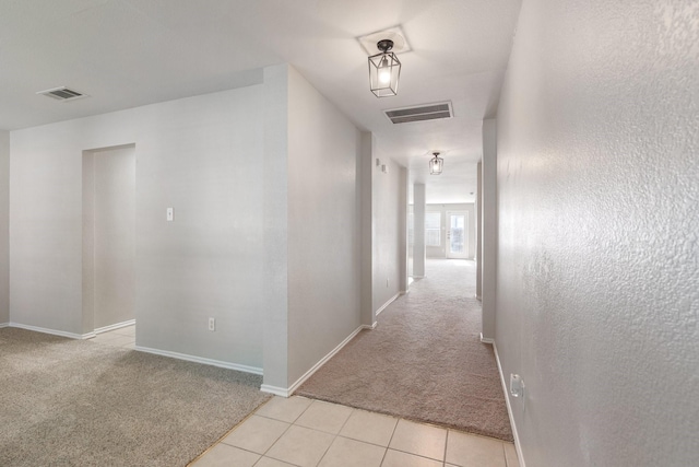 hallway featuring baseboards, visible vents, and light colored carpet