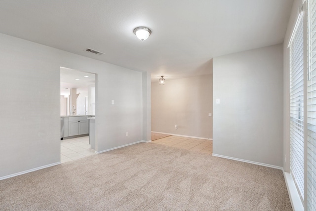 spare room featuring light tile patterned flooring, visible vents, light carpet, and baseboards
