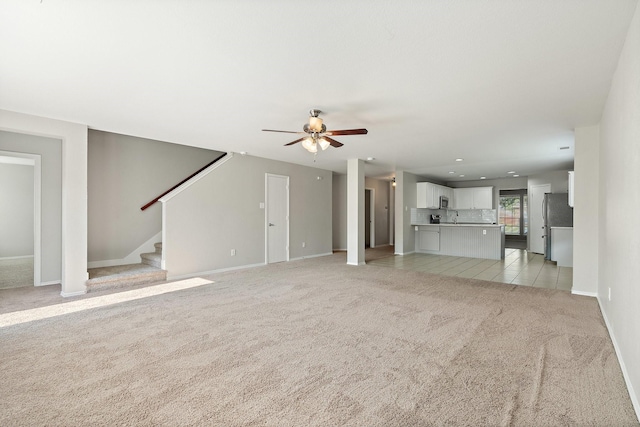 unfurnished living room featuring stairway, light tile patterned floors, a ceiling fan, light carpet, and baseboards