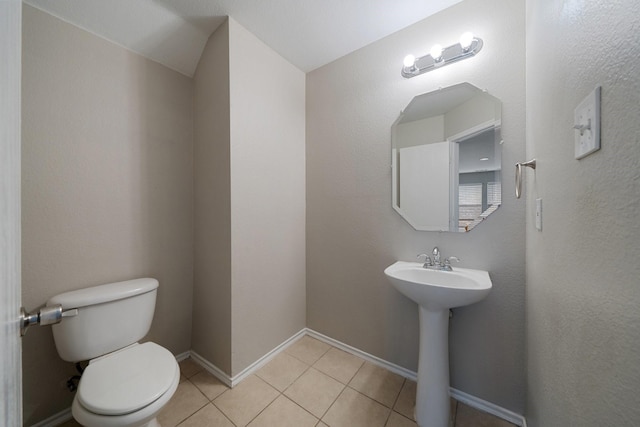 half bath featuring baseboards, toilet, and tile patterned flooring