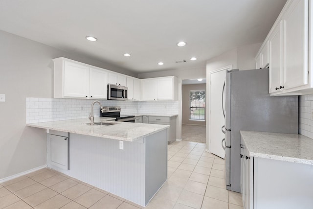 kitchen with a sink, stainless steel appliances, light tile patterned flooring, a peninsula, and backsplash