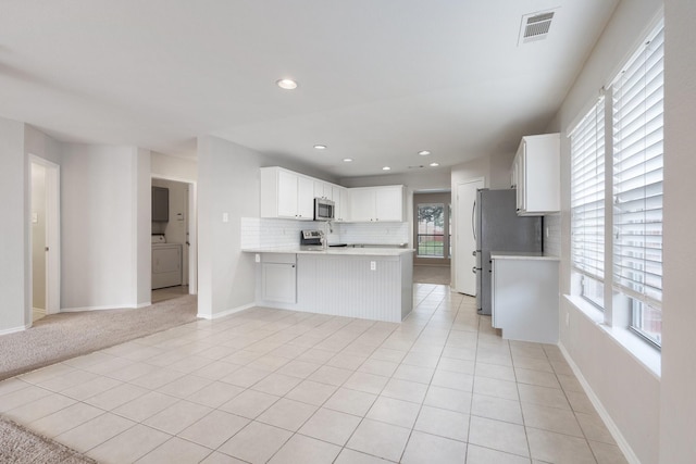 kitchen with appliances with stainless steel finishes, visible vents, light countertops, a wealth of natural light, and washer / dryer