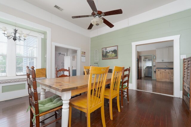 dining room featuring dark wood-type flooring, wooden walls, visible vents, washer / clothes dryer, and ceiling fan with notable chandelier