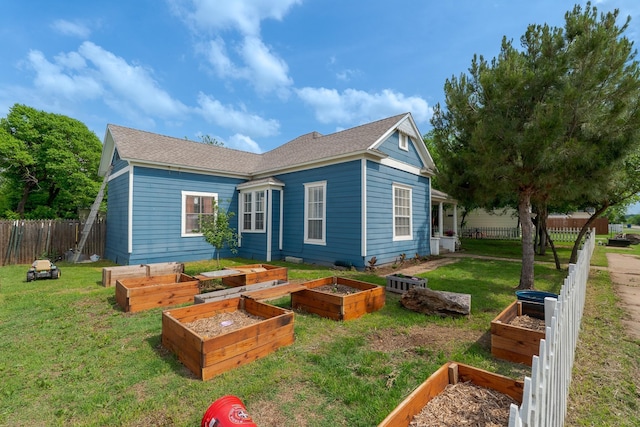 back of property featuring a lawn, fence, roof with shingles, and a garden