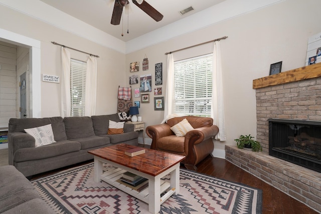living room featuring a fireplace, a ceiling fan, visible vents, baseboards, and wood finished floors