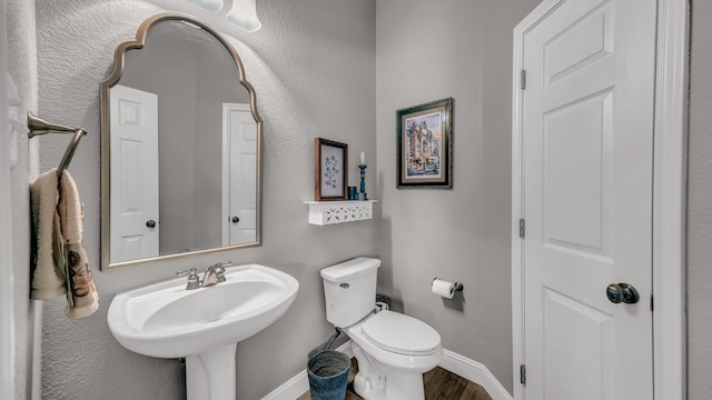 half bathroom with a sink, wood finished floors, toilet, and baseboards