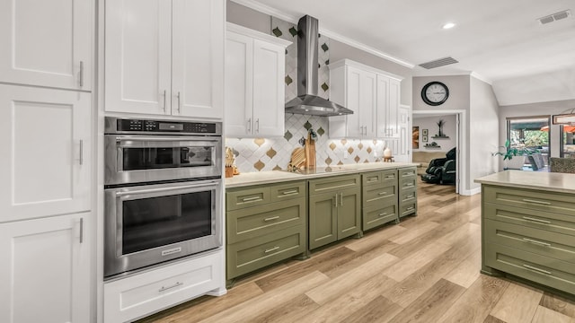 kitchen with stainless steel double oven, green cabinets, crown molding, wall chimney exhaust hood, and white cabinetry
