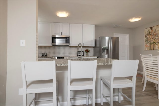 kitchen with tasteful backsplash, a sink, light stone counters, white cabinets, and stainless steel appliances