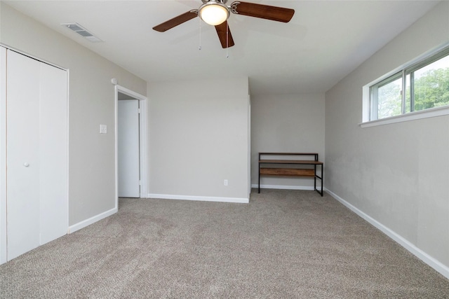 carpeted spare room featuring ceiling fan, visible vents, and baseboards