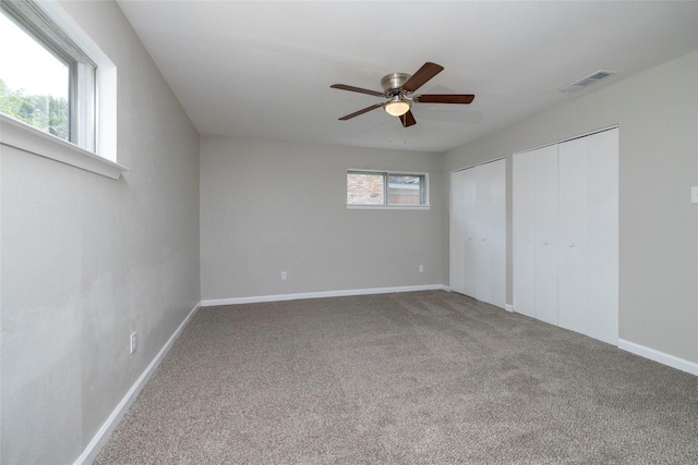 unfurnished bedroom featuring multiple closets, carpet, a ceiling fan, baseboards, and visible vents