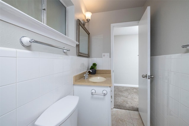 half bathroom with vanity, wainscoting, toilet, and tile walls