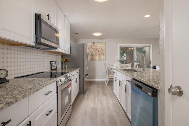 kitchen featuring white cabinets, appliances with stainless steel finishes, a sink, baseboards, and light wood-type flooring