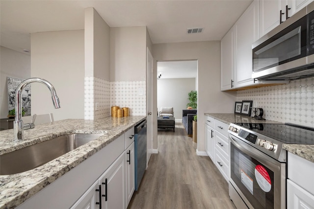 kitchen with appliances with stainless steel finishes, a sink, light wood finished floors, white cabinetry, and visible vents