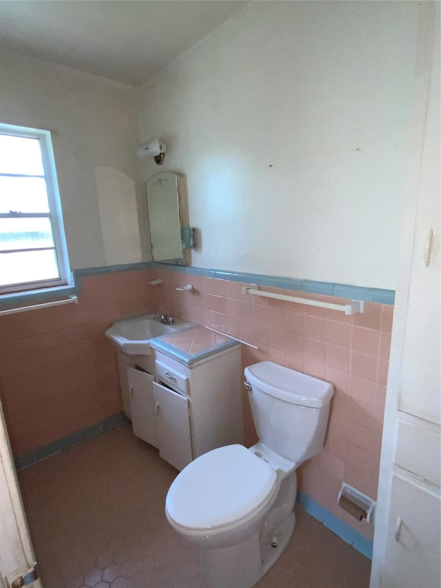 bathroom featuring tile patterned flooring, wainscoting, tile walls, toilet, and vanity
